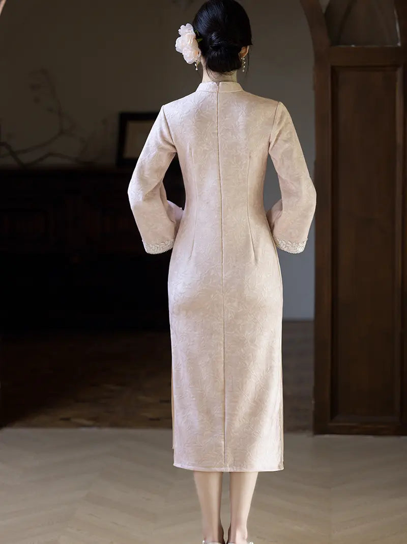 A woman viewed from behind wearing a light beige, long-sleeved cheongsam-style dress with a subtle textured pattern, standing in a dimly lit indoor setting.