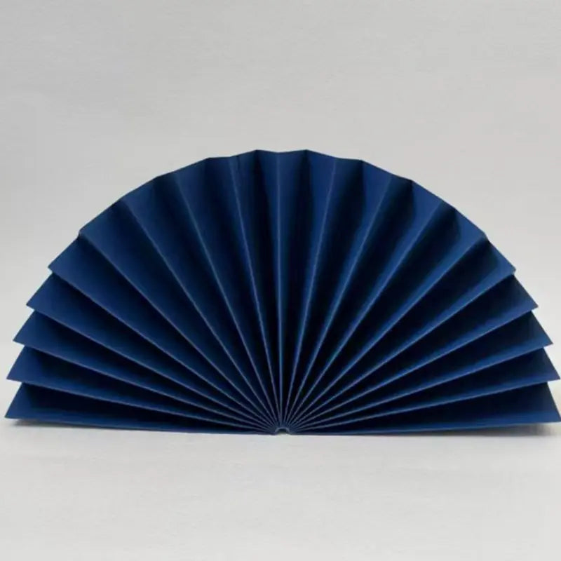 A dark blue pleated paper fan, partially unfolded, displayed against a neutral light gray background.