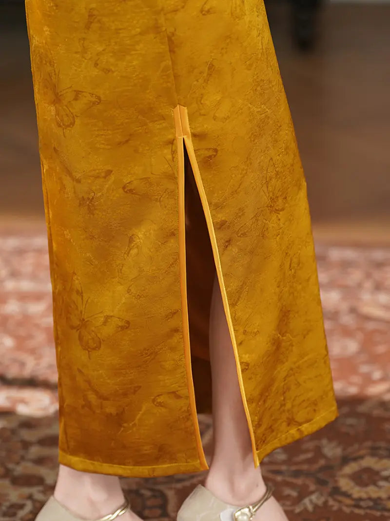 Close-up of a person wearing a mustard yellow Pearl-Trimmed Sleeveless Halter Jacquard Satin Qipao  with a front slit, paired with light-colored flat shoes, standing on a patterned rug.