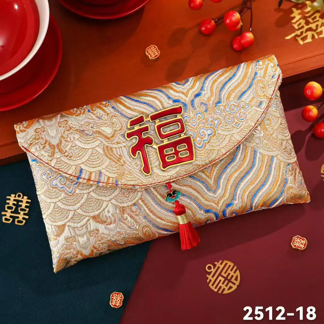 A Chinese New Year red envelope clutch bag made of brocade fabric with a red embroidered Chinese character 'Fu' on the front flap, decorated with a red tassel. The bag is styled on a dark red wooden table alongside red dishes, decorative double happiness symbols, and red fruits.
