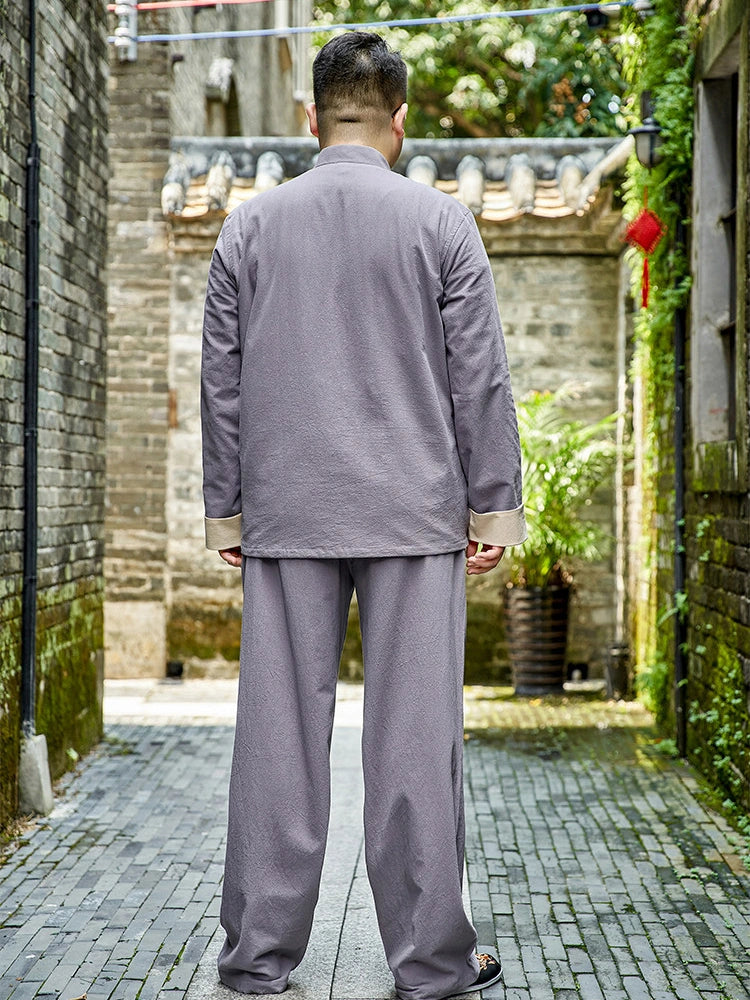 A man viewed from behind wearing a light gray plus size traditional Chinese-style two-piece outfit with beige cuffs, standing in a narrow stone alleyway.