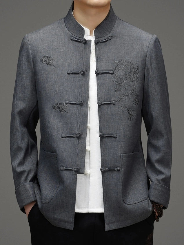 A man wearing a gray traditional Chinese-style jacket with frog closures and dragon embroidery, layered over a white shirt and black pants.