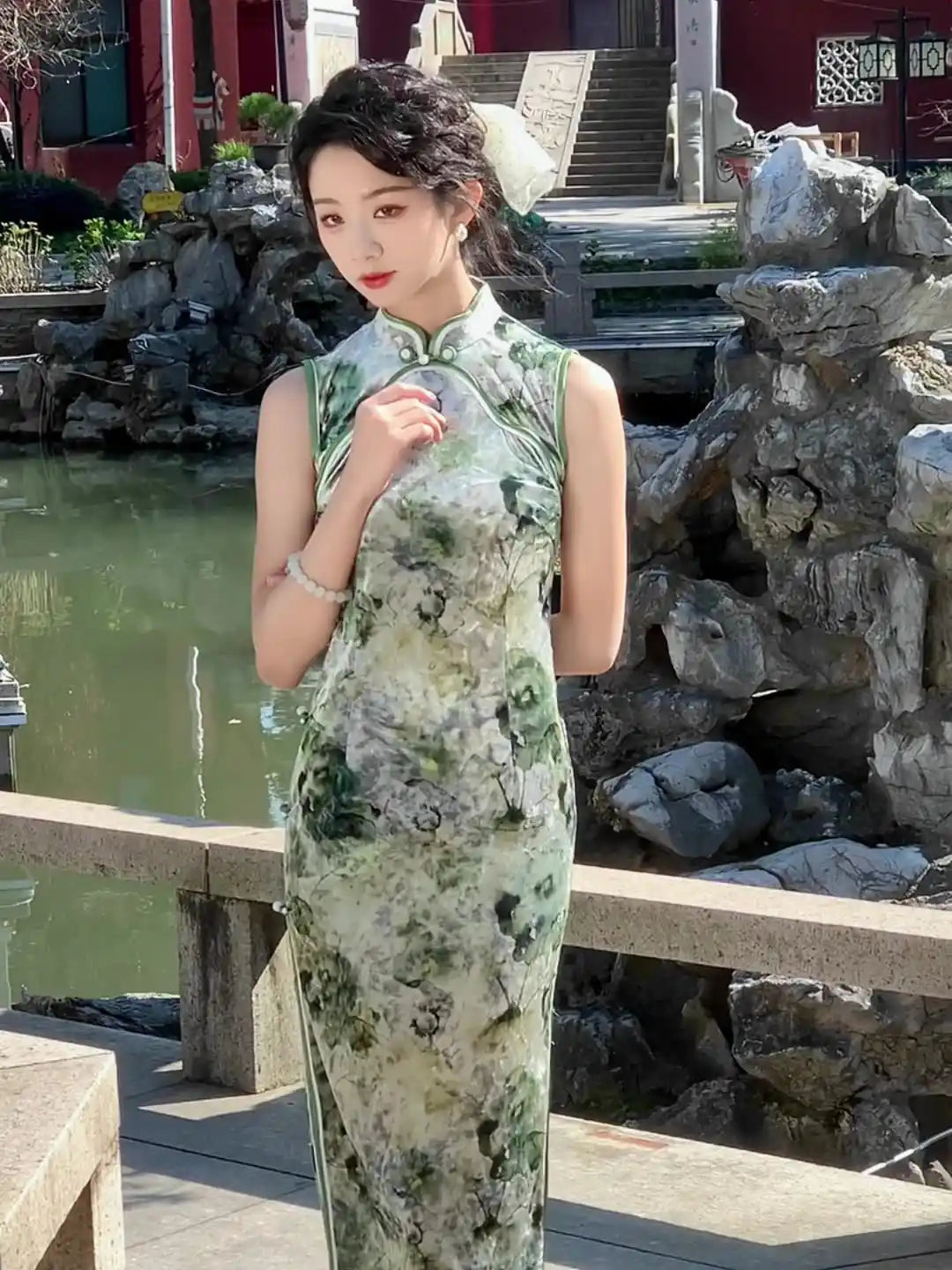 Woman in a green  Floral Sleeveless Velvet Qipao Dress standing in a scenic outdoor setting with rocks and water.
