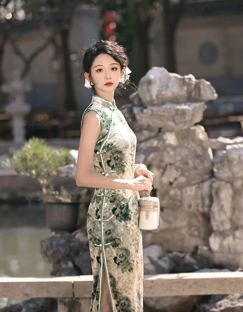 Woman in a green  Floral Sleeveless Velvet chinese cheongsam Qipao Dress holding a cup in an outdoor setting with rocks and plants.
