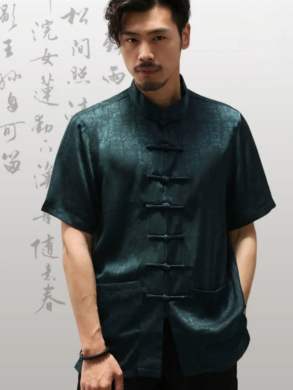 Man wearing a dark green traditional  Men's Luxury Mulberry Silk Jacquard Short Sleeve Tang Shirt outfit with Chinese calligraphy in the background