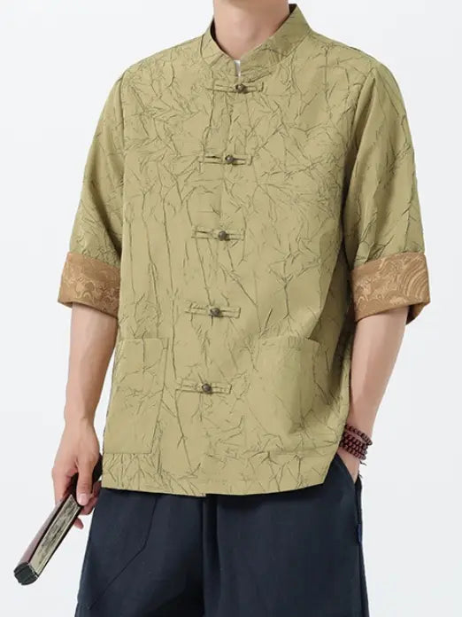 Person wearing a patterned green Men's Retro Crinkle Texture Half Sleeve Tang Suit Summer Shirt with rolled-up sleeves on a white background