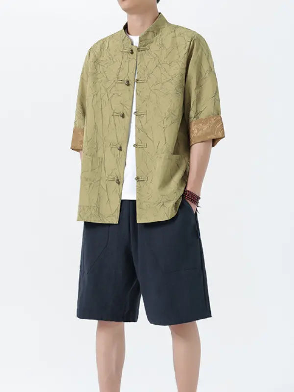 Person wearing a green textured Men's Retro Crinkle Texture Half Sleeve Tang Suit Summer Shirt and dark shorts on a white background