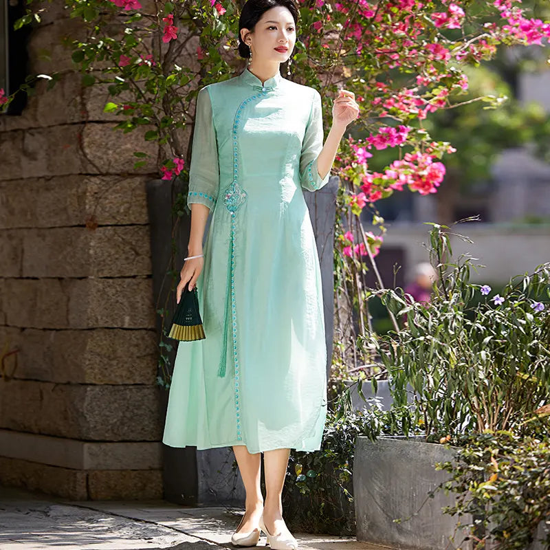 Woman in a light green Modern A-Line Tencel Jacquard Loose Cheongsam Qipao Dress standing outdoors with pink flowers and plants in the background