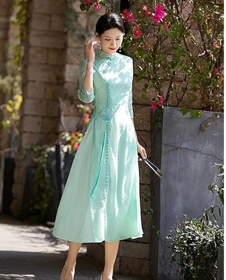 a chinese Woman in a light green Modern A-Line Tencel Jacquard Loose Cheongsam Qipao Dress  standing outdoors with flowers and a stone wall in the background
