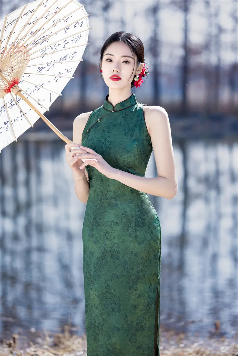 Woman in a green Modern Chinese Mandarin Dress Sleeveless Qipao  holding a traditional umbrella with a blurred natural background