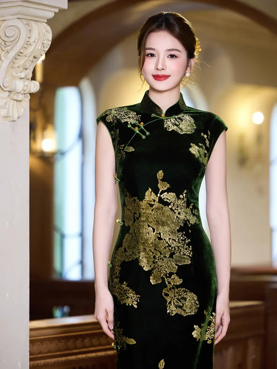 A woman wearing a dark green velvet cheongsam with gold floral embroidery, standing in a warmly lit indoor setting with classical columns.