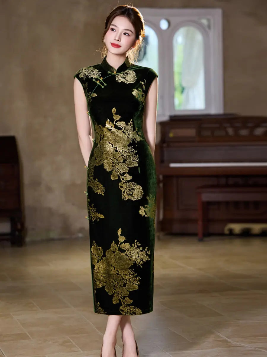 A woman modeling a sleeveless green velvet cheongsam dress with gold floral embroidery, standing in a softly lit indoor room with a piano in the background.