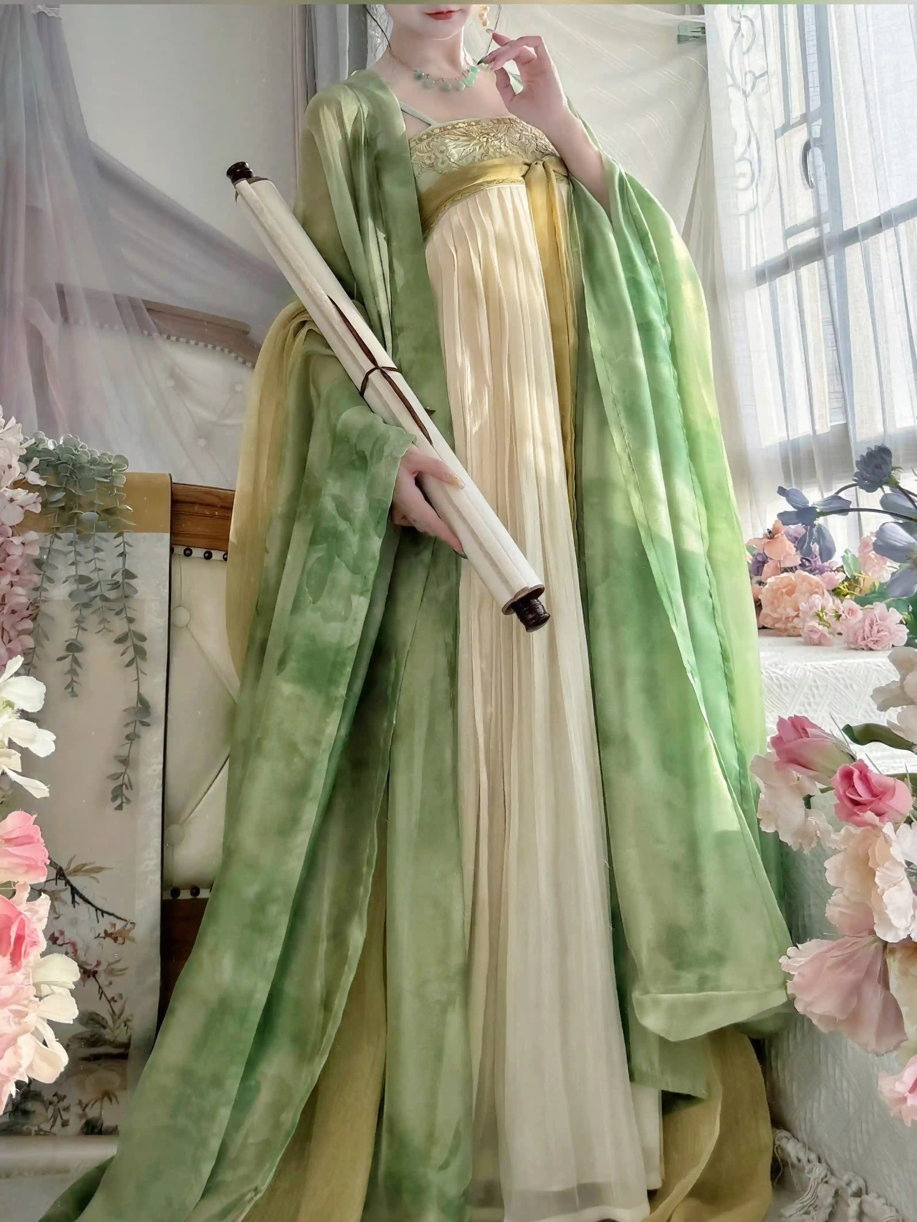 A woman wearing a traditional Chinese tang dynasty Hanfu-style dress in cream and light green, holding a rolled scroll. The dress features a cream-colored skirt and bodice with a light green outer layer.