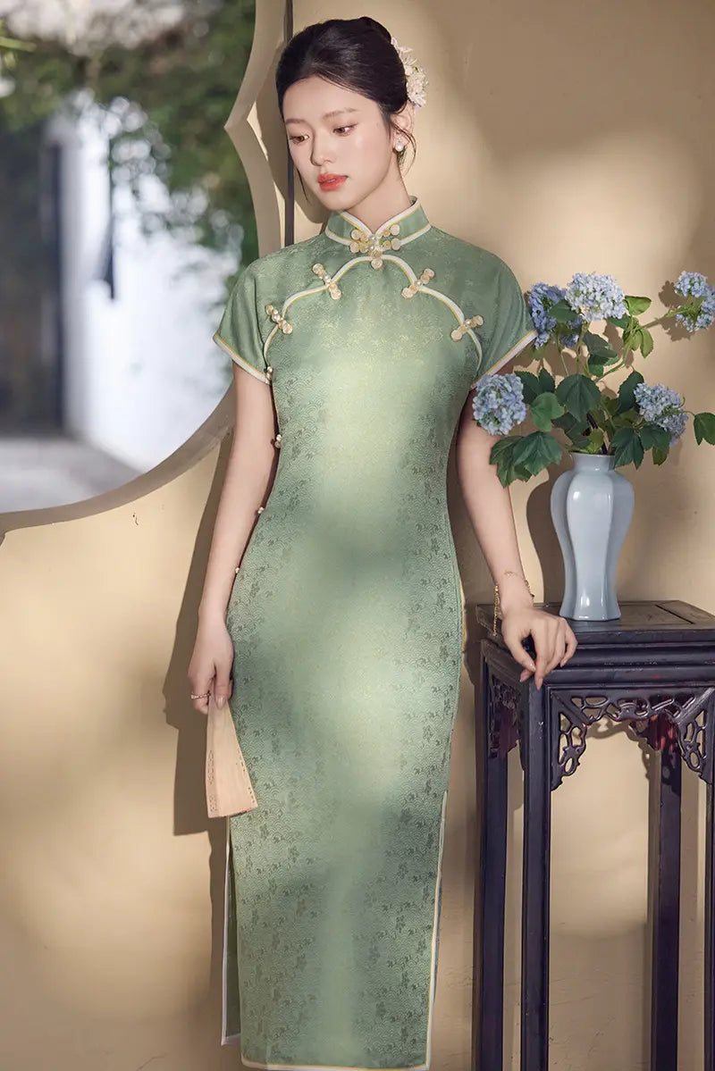 Woman in a  green traditional  Song Brocade Full-Opening  Qipao Dress standing next to a table with a vase and flowers.