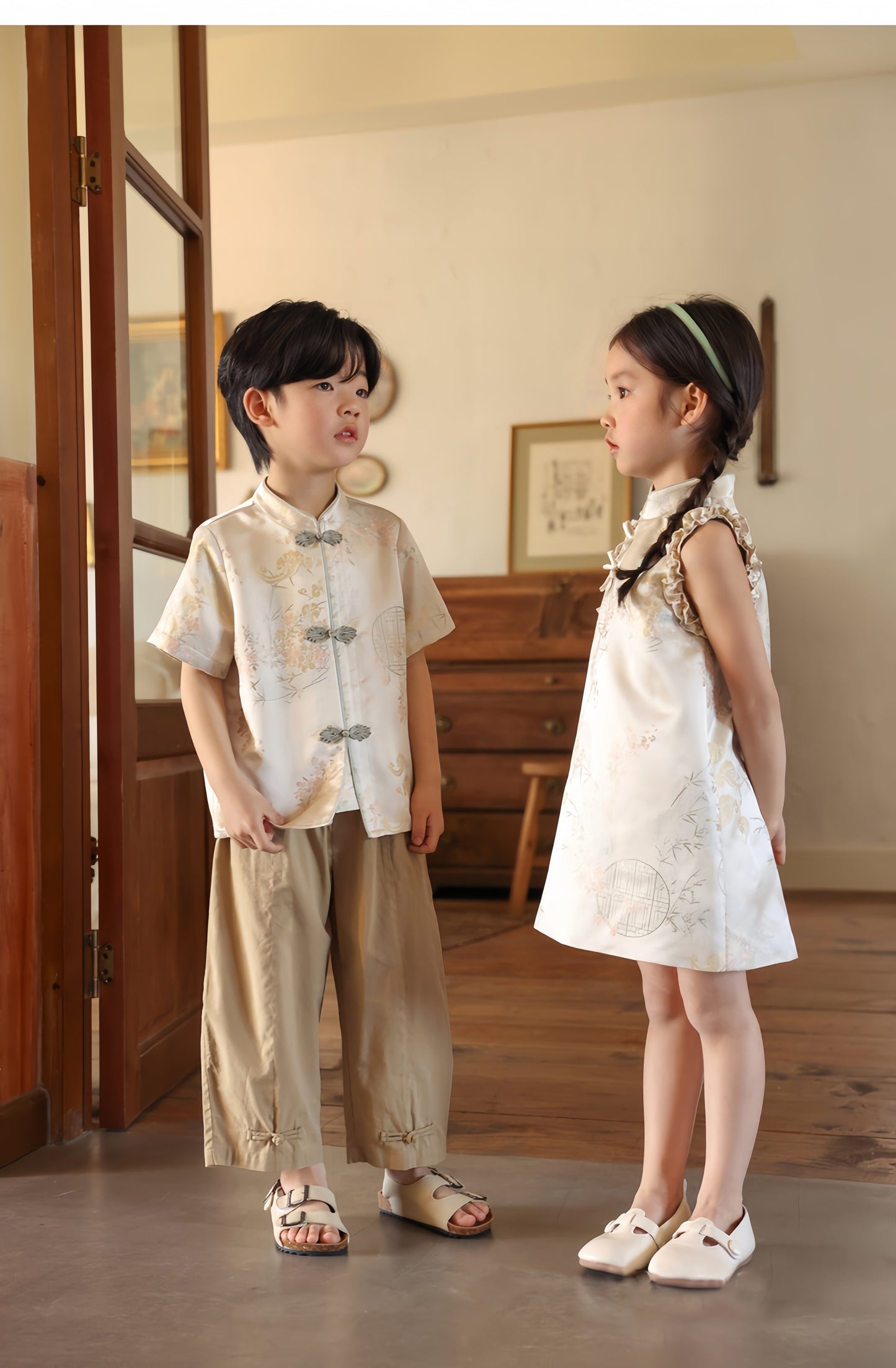 A chinese kid girl in white qipao dress and a chinese boy kid in matching white tang jacket standing