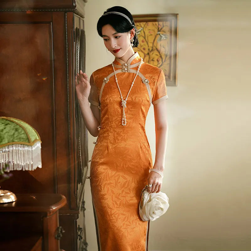 Woman in an l Golden  orange Chinese  long cheongsam evening gown dress  standing next to a wooden cabinet.