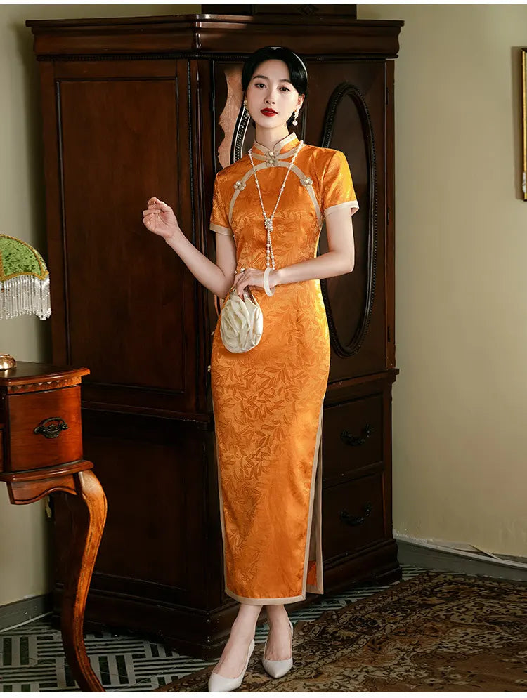 Woman in  Golden  orange Chinese  long qi pao dress  standing in a room with wooden furniture.