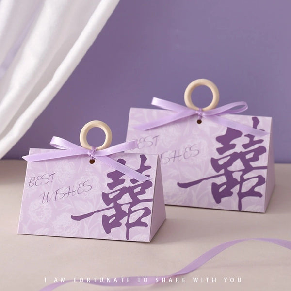 Two purple Floral Triangular Shape Double Happiness Favor Boxes  with ribbons and Chinese characters on a light purple background.