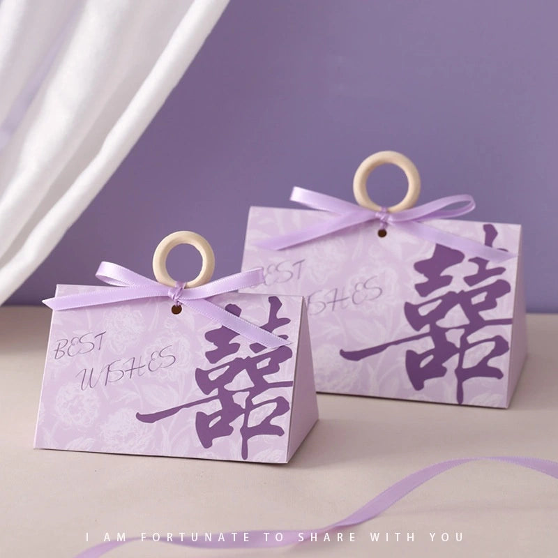 Two purple Floral Triangular Shape Double Happiness Favor Boxes  with ribbons and Chinese characters on a light purple background.