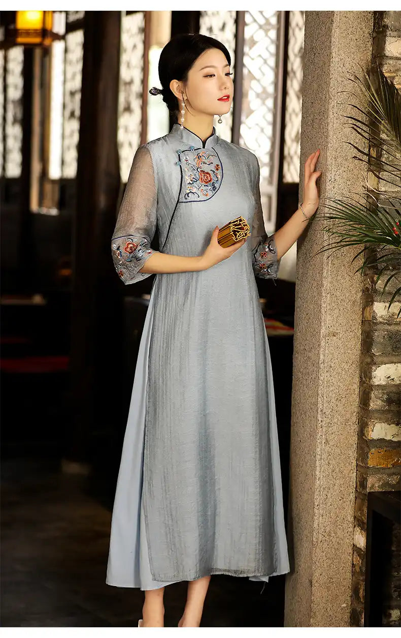 Woman in a Modern A Line Loose Cheongsam Qipao Dress with Sheer Sleeve  traditional dress with floral embroidery standing against a stone wall.