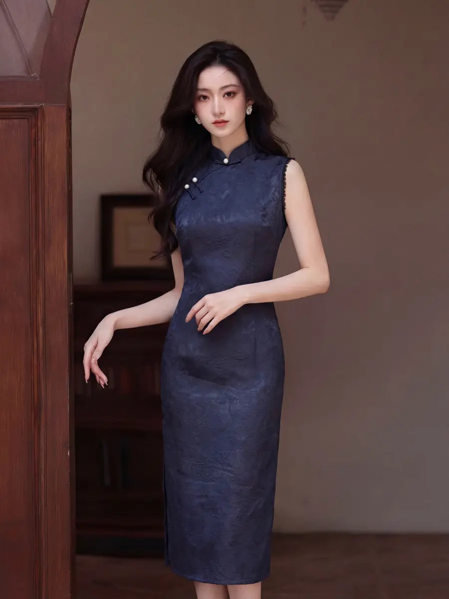 A woman modeling a sleeveless dark blue textured cheongsam-style dress with a high collar and decorative buttons, standing in an indoor setting with a warm brown background.