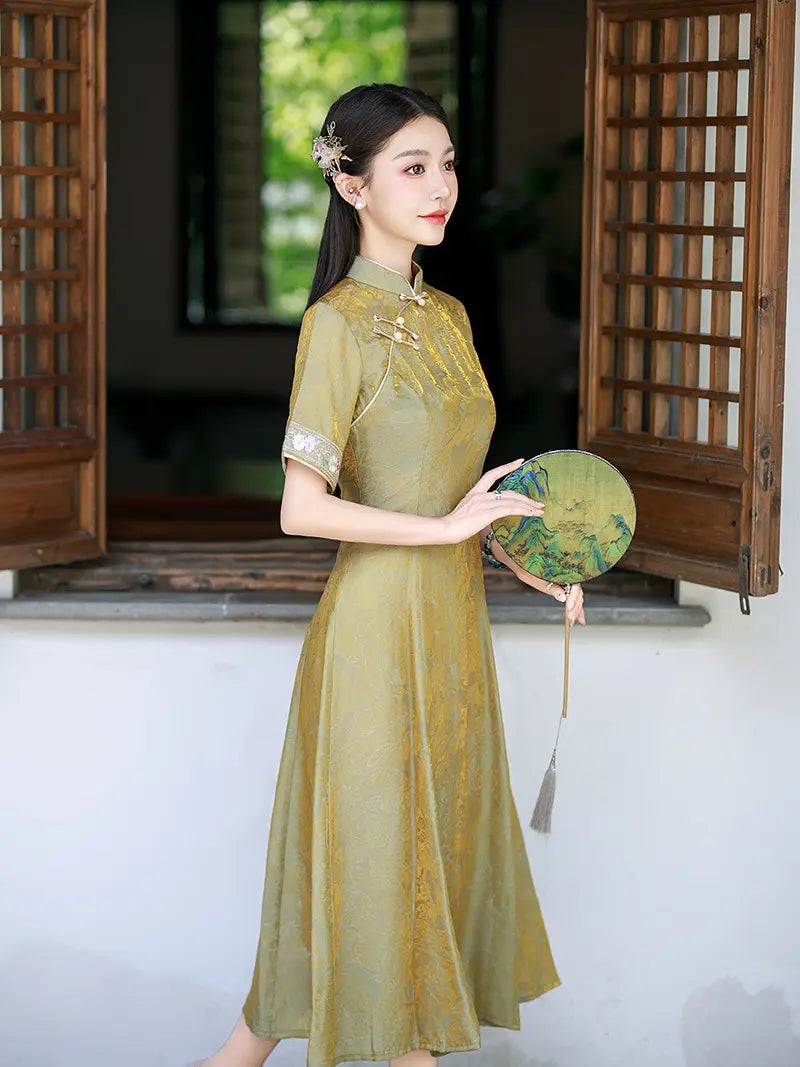 A woman wearing a traditional Chinese a line cheongsam dress in olive green, holding a round fan in front of a wooden lattice window.