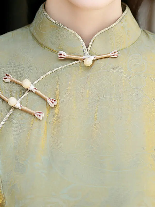 Close-up of a person wearing a pale yellow-green traditional Chinese cheongsam qipao  with decorative wooden and fabric frog closures on the collar and chest.