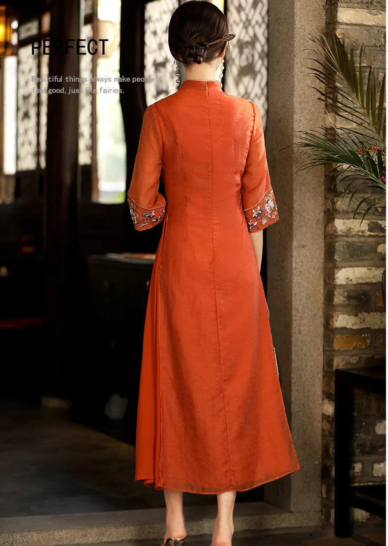 Woman wearing an orange dress with intricate details in a room with stone walls and plants.