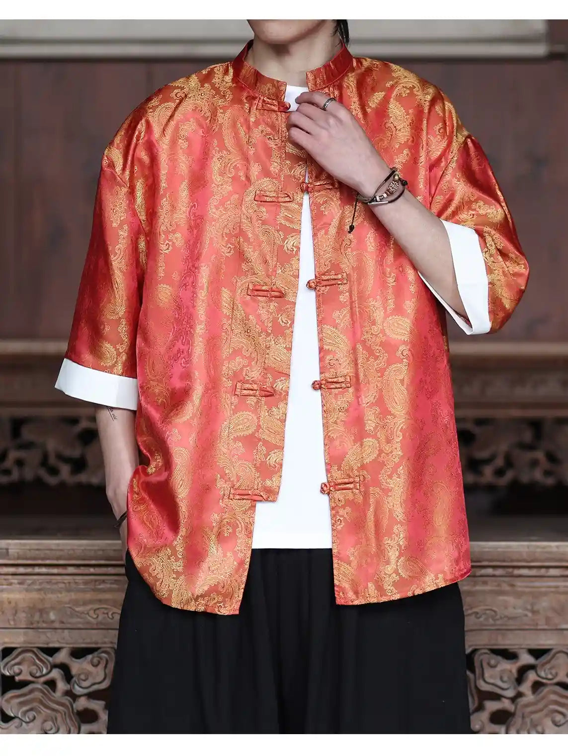 Person wearing a orange  and gold traditional Modern New Chinese Style Men's Half Sleeve Jacquard Tang Shirt  with a white shirt underneath, standing against a wooden background.