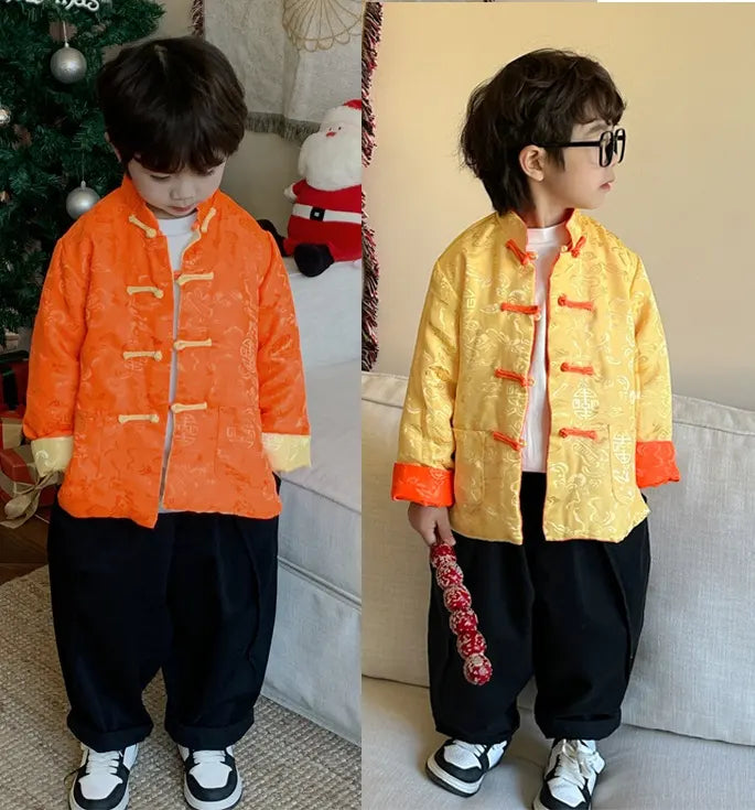 Two children wearing orange yellow Traditional Chinese Kid's Reversible Tang Jacket outfits in orange and yellow, standing in a room with a Christmas tree and decorations.