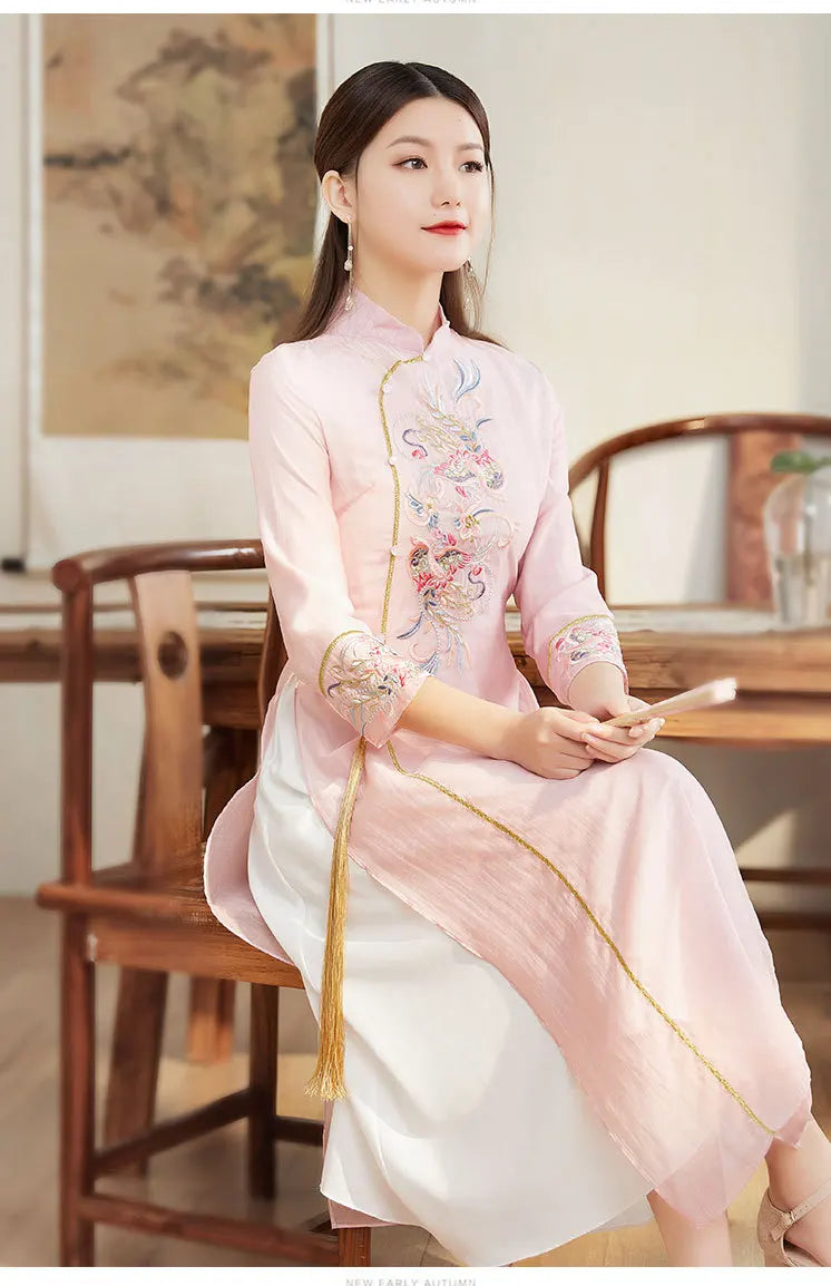 Woman in a traditional embroidered pink Ao Dai Style Qipao Dres – A-Line Long Cheongsam  sitting in a room with wooden furniture.