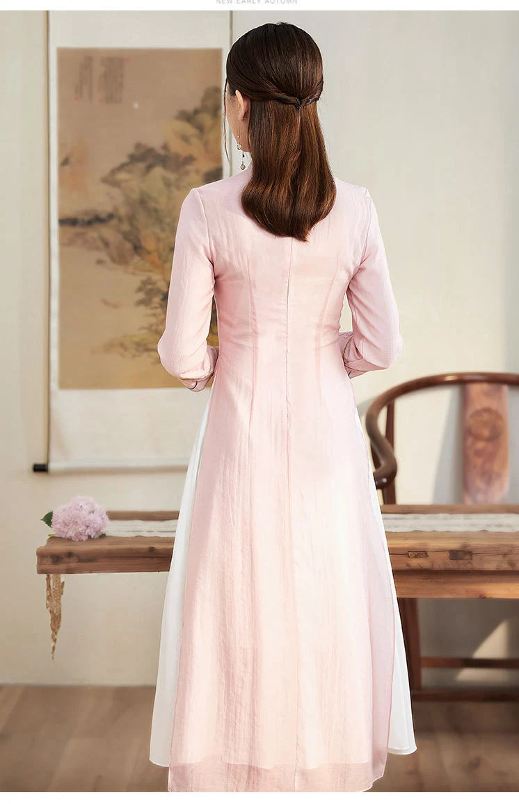 Woman wearing a light pink traditional  Ao Dai Style Qipao Dres – A-Line Long Cheongsam  in a room with wooden furniture and a painting.