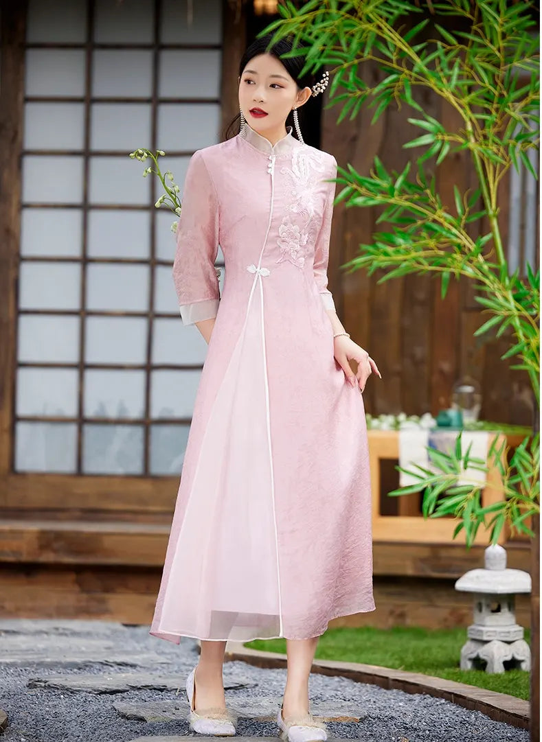 Woman in a Floral Embroidered Loose A line pink Cheongsam Qipao Dress standing in a garden setting with plants and a stone lantern.