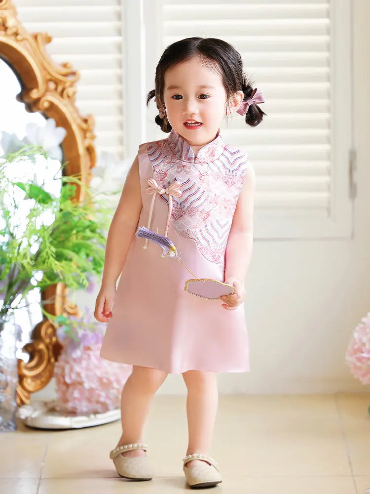 Young girl in a pink Girls' "Good Fortune" Traditional Sleeveless A-Line Jacquard Qipao  dress standing in a decorated room with flowers and a mirror.
