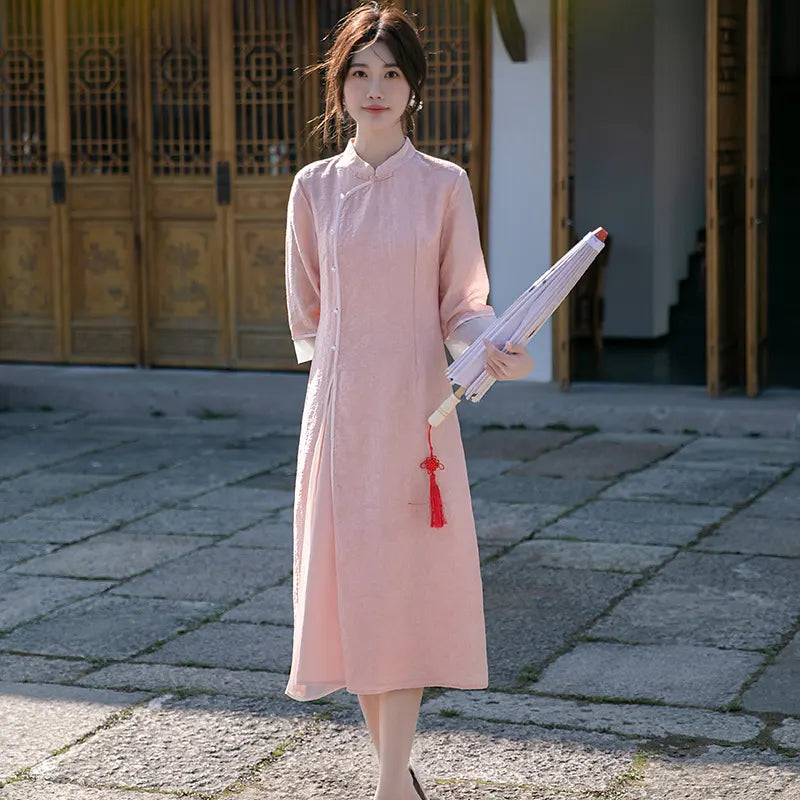 Woman in a long pink dress holding an umbrella with a red tassel in front of traditional architecture.