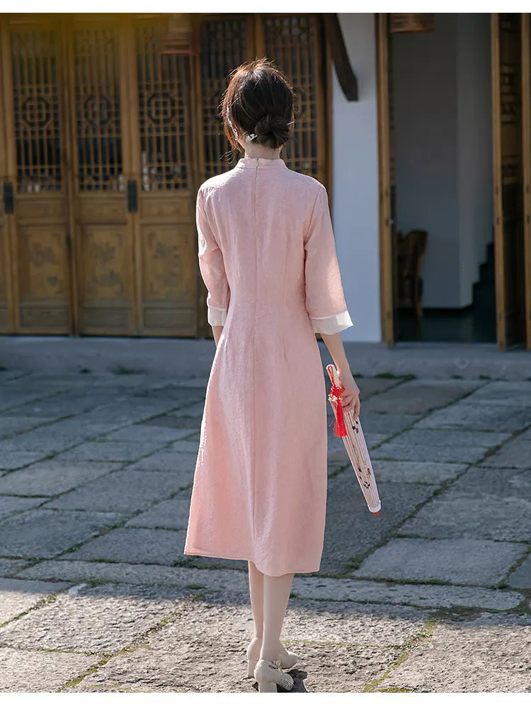 Woman in a pink Loose A Line Cheongsam Qipao Dress  holding a red and white object, standing on a stone pavement.