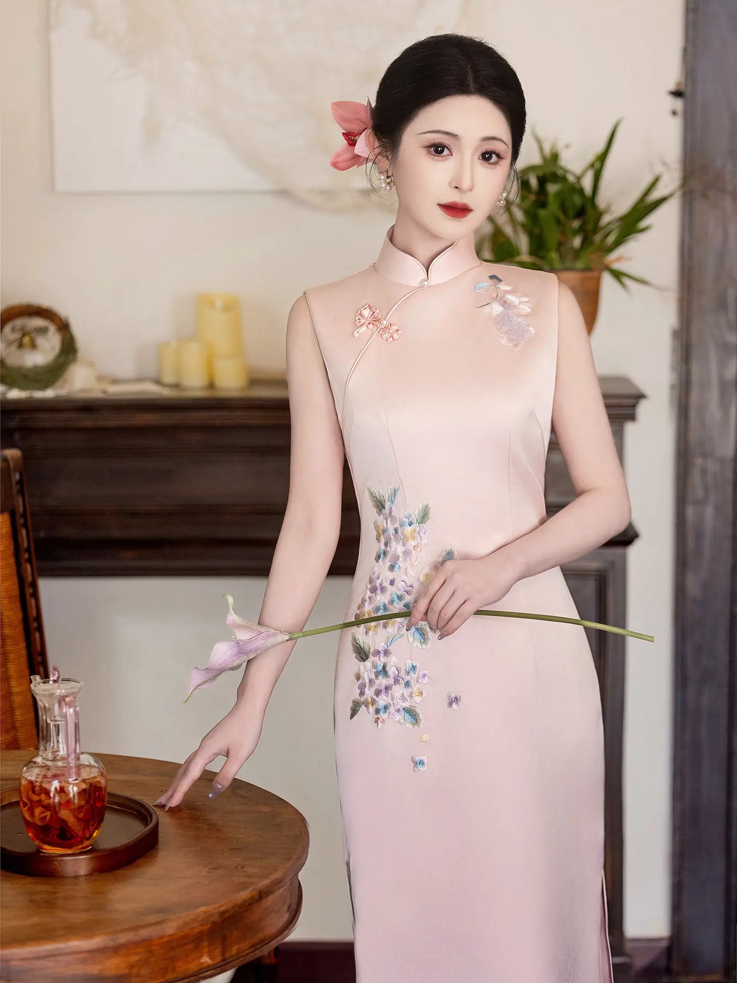 Woman in a traditional light pink Luxury Embroidered New Chinese Style Sleeveless Qipao cheongsam Dress with floral embroidery, holding a flower, in an elegant interior setting.