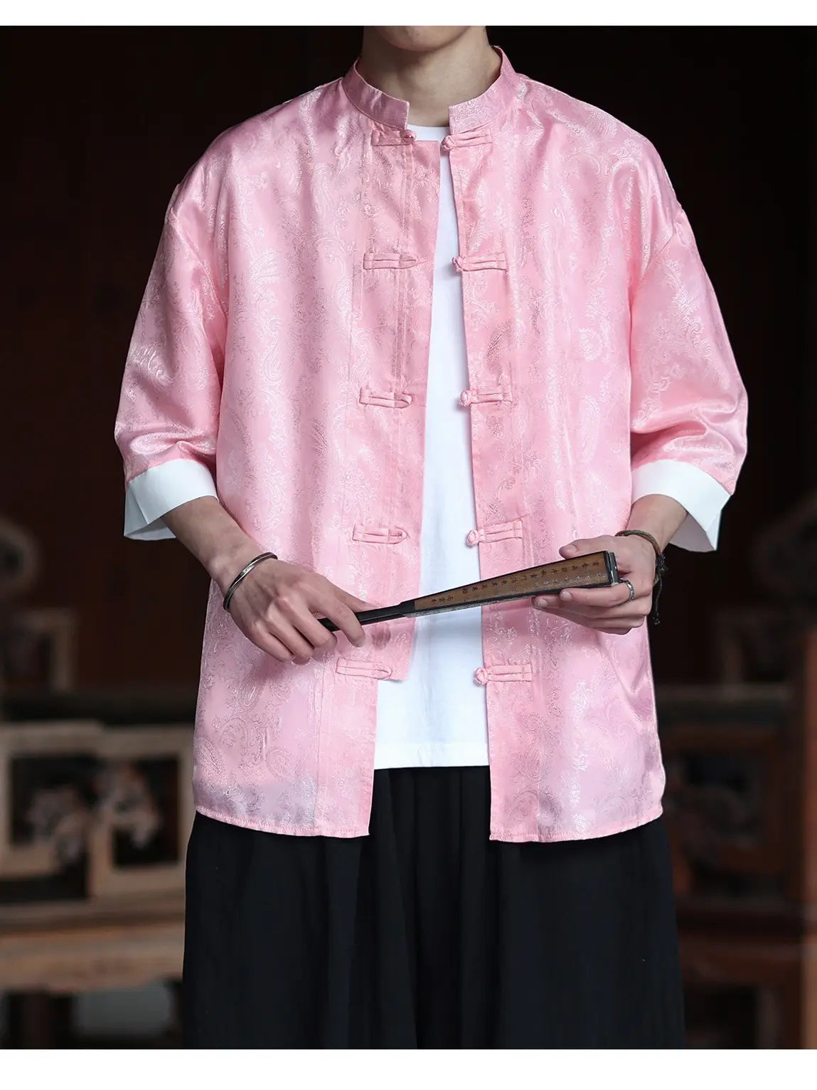 Person wearing a pink traditional  Modern New Chinese Style Men's Half Sleeve Jacquard Tang Shirt jacket holding a book in a blurred indoor setting