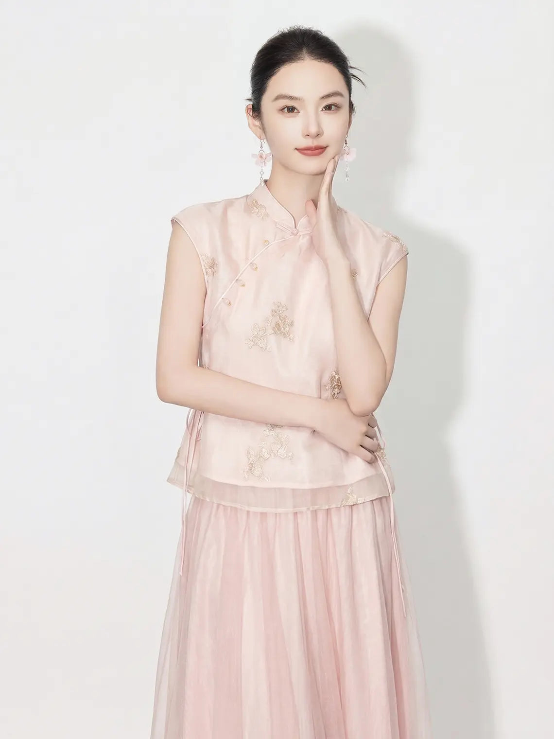 Woman wearing a light pink traditional New Chinese Style - Sleeveless Asymmetric Top & Maxi Skirt Set outfit with floral patterns on a white background