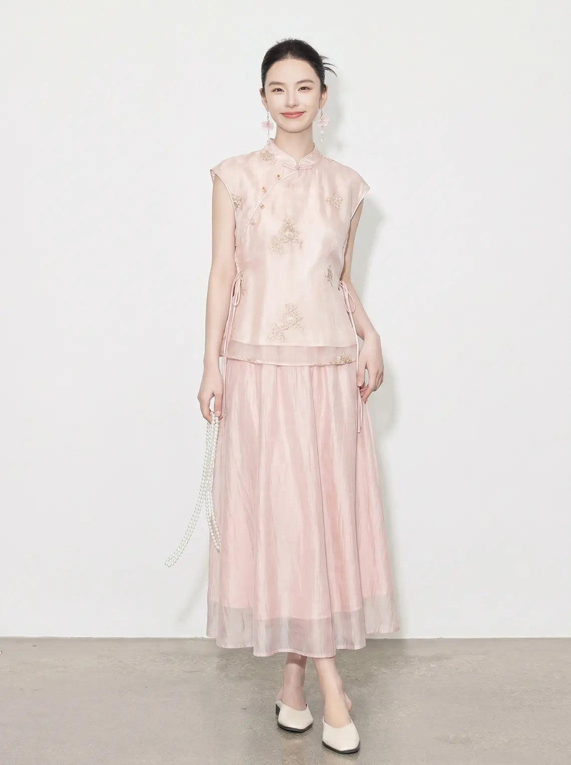 Woman wearing a light pink New Chinese Style - Sleeveless Asymmetric Top & Maxi Skirt Set dress against a white background