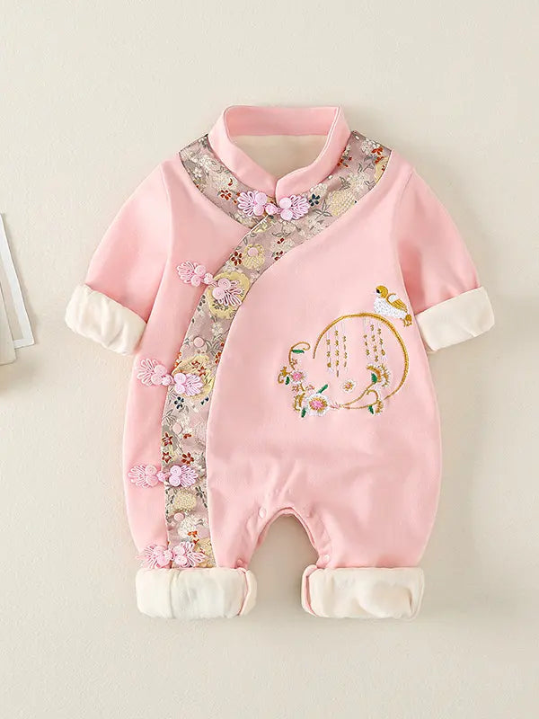 A pink Traditional Chinese Embroidered Baby Girl Qipao Romper  with a traditional Chinese cheongsam design, featuring floral embroidery, decorative frog closures, and white contrast cuffs, displayed against a light beige background.
