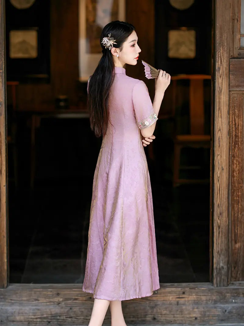 A woman wearing a lavender pink traditional Chinese cheongsam dress with gold embroidery, standing in a doorway of a rustic wooden building.