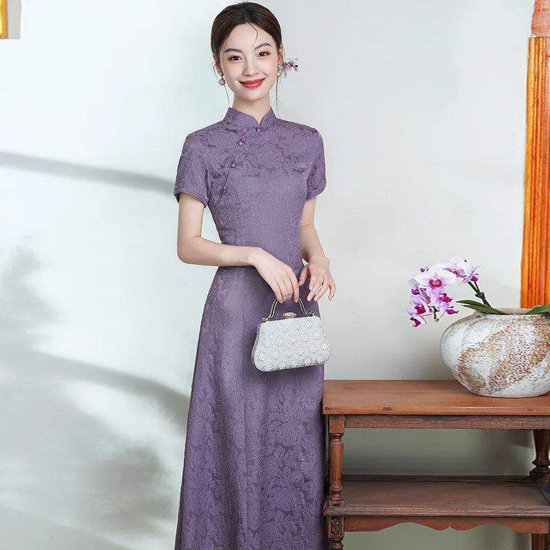 Woman in a purple  Short Sleeve Floral A Line Qipao cheongsam  holding a white handbag, standing next to a wooden table with a vase and flowers.