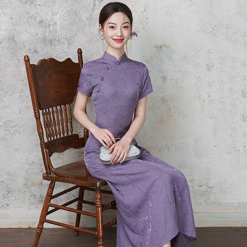Woman in apurple  Short Sleeve Floral A Line Qipao cheongsam  sitting on a wooden chair against a textured wall.
