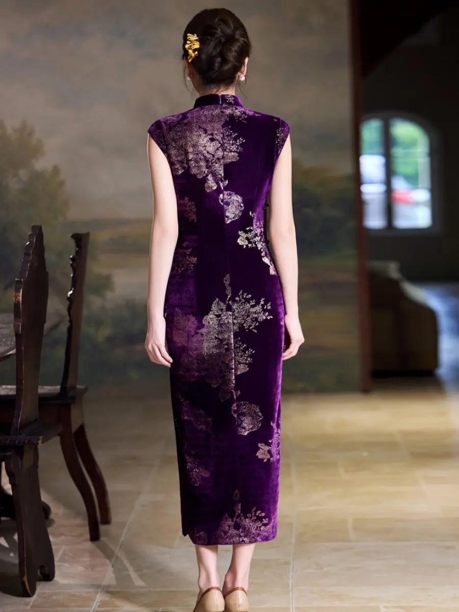 A woman viewed from behind wearing a sleeveless purple cheongsam dress with a floral pattern, standing in an indoor room with a painted wall and chairs visible.