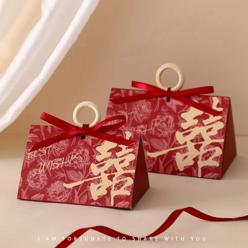 Two red Floral Triangular Shape Chinese wedding Double Happiness Favor Boxes gift boxes with floral patterns and ribbons on a beige background