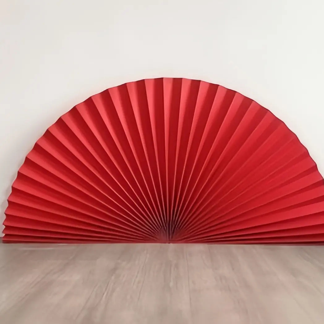 A red pleated accordion backdrop panel, partially unfolded, standing on a light gray wood floor against a plain white wall.