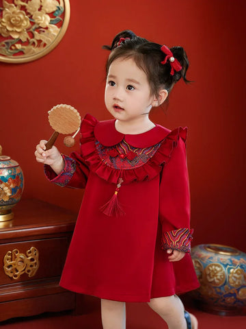 Child in a red traditional Modern Chinese Baby girl Qipao Cheongsam Dress with Tassel outfit holding a fan against a red background
