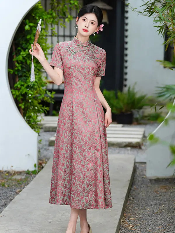 Woman in a pink Modern Floral Short Sleeve A-Line Qipao Dress  holding a fan in an outdoor setting with greenery.