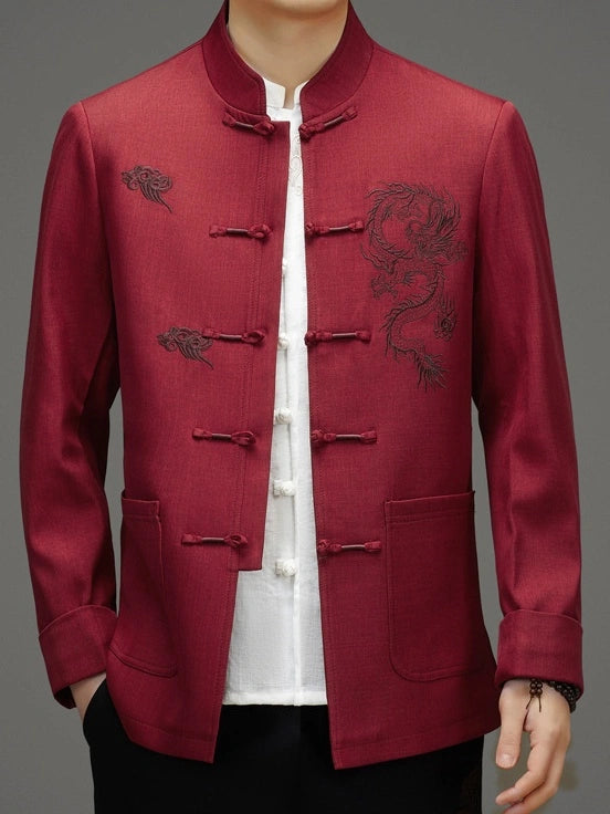 A man wearing a red Chinese-style jacket with dragon embroidery on the chest, featuring traditional frog closures and a mandarin collar, layered over a white shirt.